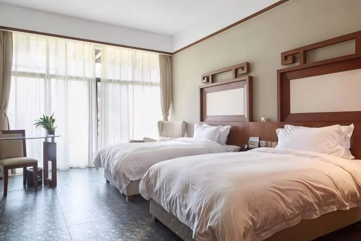 A hotel room with two beds, a desk, a chair, and a large window with curtains.