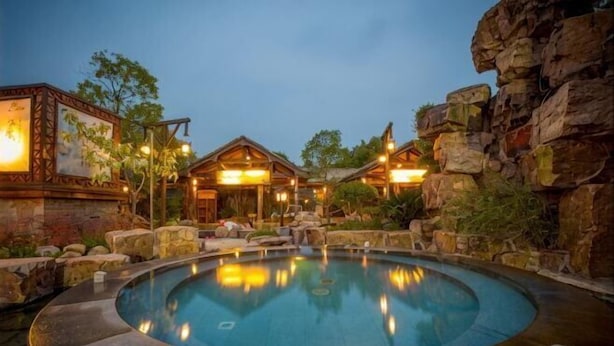 Un área de piscina con jacuzzi, paredes de piedra y estructuras de madera.