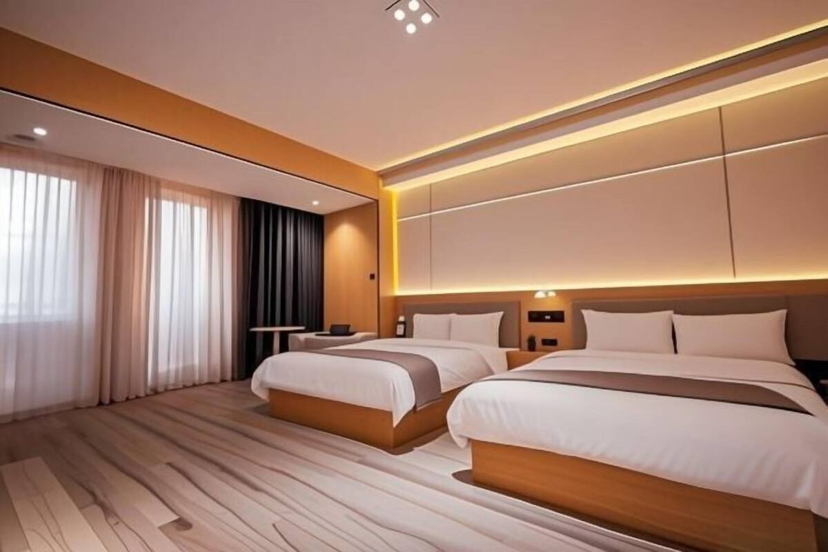 Une chambre d’hôtel moderne avec deux lits, une grande fenêtre avec des rideaux, un plancher en bois et un téléviseur fixé au mur.