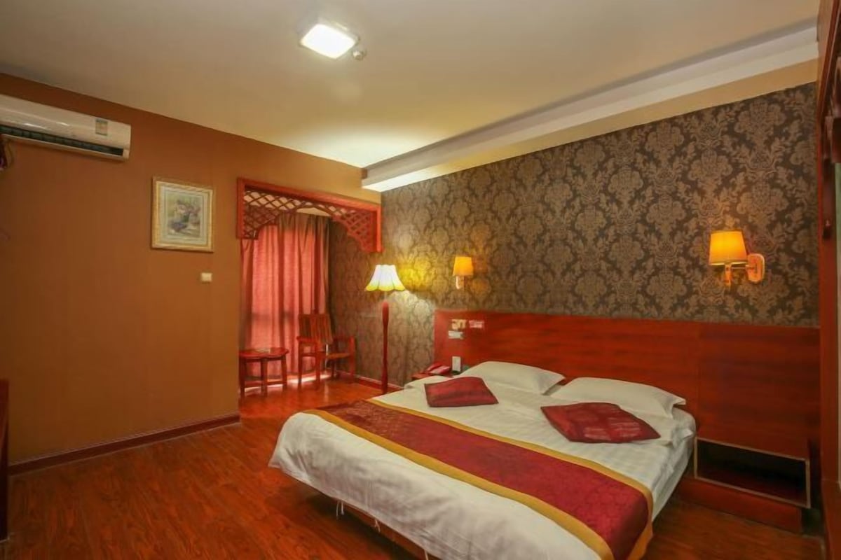 Een hotelkamer met een houten bed, twee bedlampen, een rood gordijn en behang met een patroon.