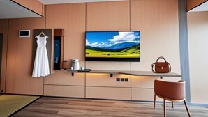 Quarto moderno com TV de tela plana, um armário de madeira, um vestido pendurado e uma cadeira.