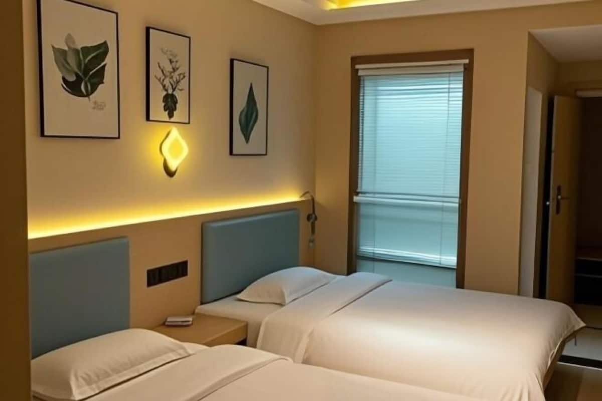 Une chambre d’hôtel avec deux lits, une table de chevet, une lampe et des reproductions encadrées de motifs botaniques accrochées au mur.
