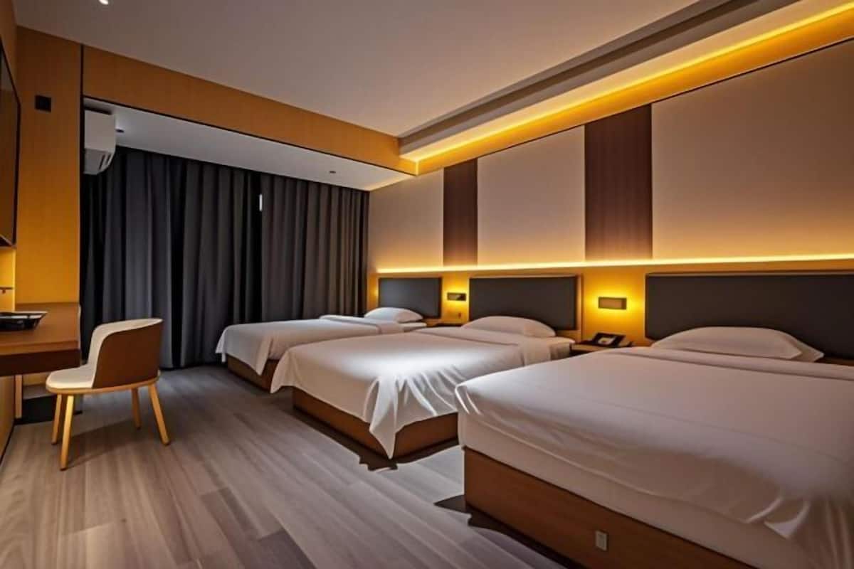 Une chambre d’hôtel avec trois lits, un bureau et une chaise.