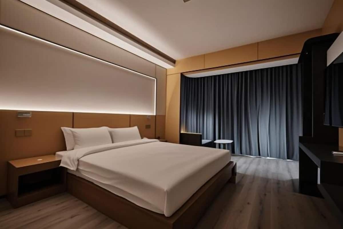 Une chambre d’hôtel moderne, dotée d’un grand lit, de tables de chevet, d’un bureau et offrant une vue sur l’extérieur.