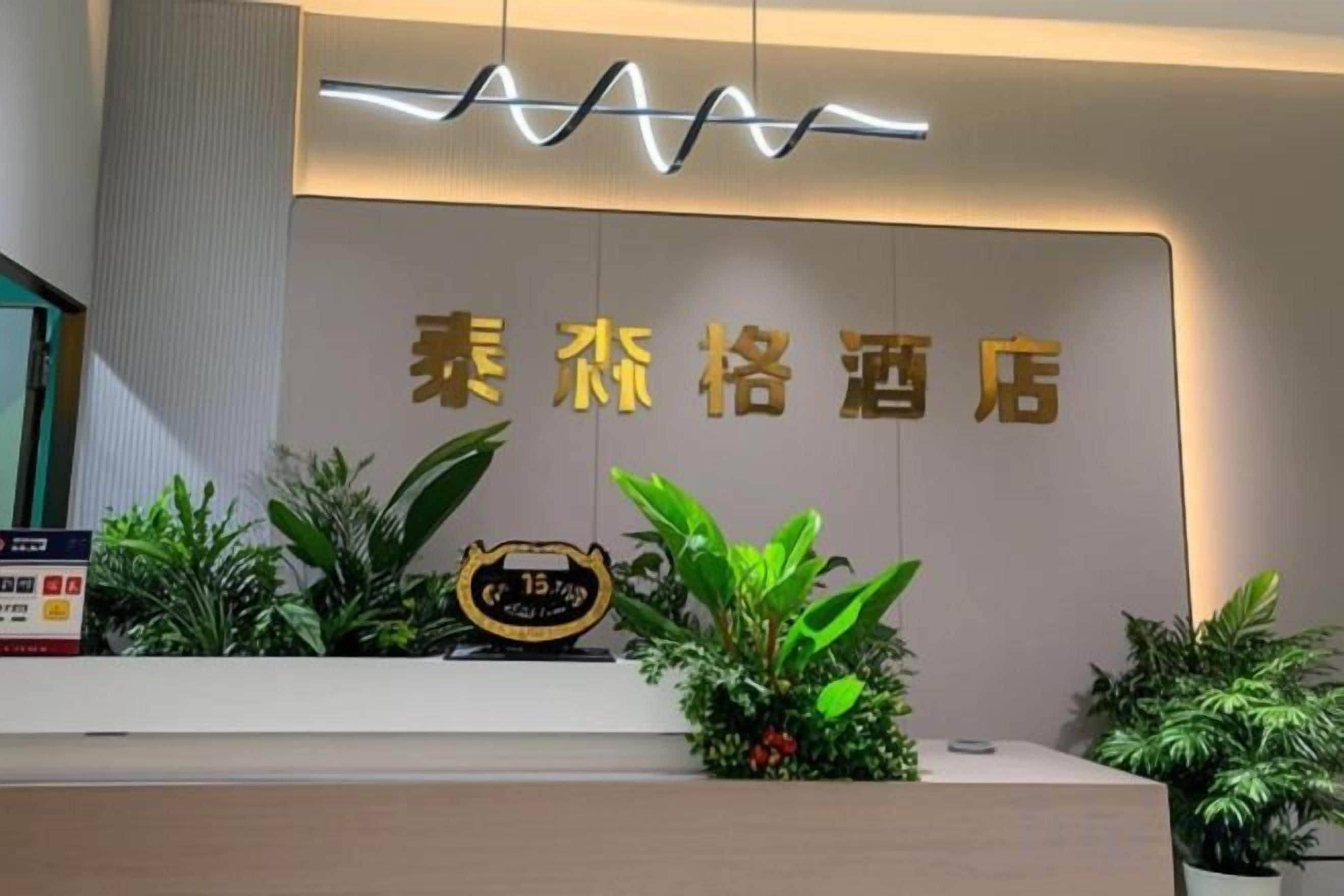 A hotel reception area with a modern design, featuring a reception desk, a wall-mounted sign with the hotel's name, and decorative plants.
