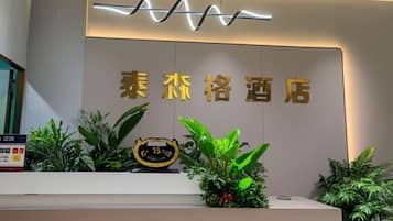 A hotel reception area with a modern design, featuring a reception desk, a wall-mounted sign with the hotel's name, and decorative plants.