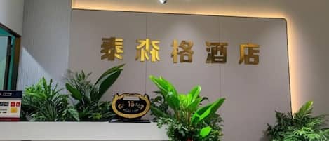 A hotel reception area with a modern design, featuring a reception desk, a wall-mounted sign with the hotel's name, and decorative plants.