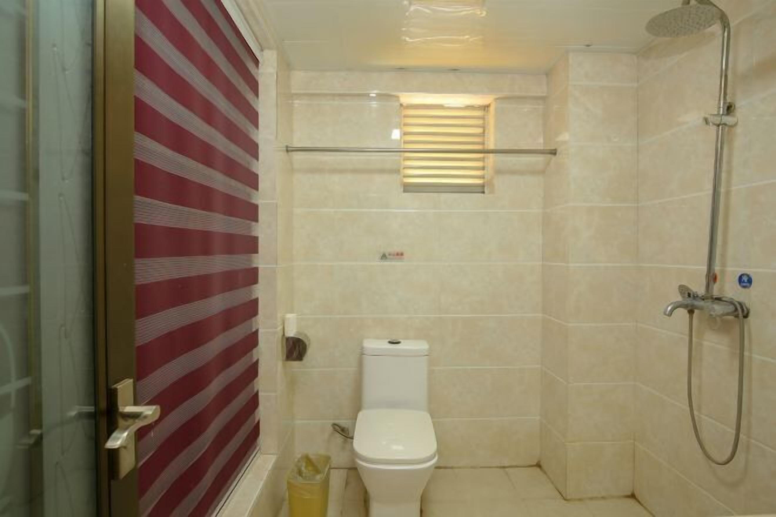 A small bathroom with a toilet, a shower, and a window with blinds.