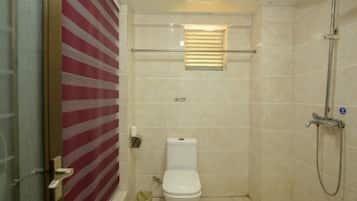 A small bathroom with a toilet, a shower, and a window with blinds.