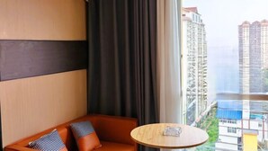 Quarto de hotel com sofá, mesa redonda e vista para edifícios altos.