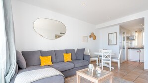 Een moderne woonkamer met een grijze bank, een salontafel en een eethoek met een witte tafel en stoelen.