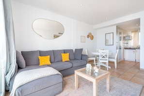 Ein modernes Wohnzimmer mit einem grauen Sofa, einem Couchtisch und einem Essbereich mit einem weißen Tisch und Stühlen.