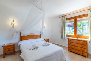 A bedroom with a bed, bedside tables, a wooden dresser, a window with curtains, and wall-mounted lights.