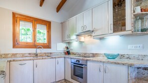 A kitchen with wooden cabinets, a built-in oven, a window with blinds, and a countertop with a bowl. - Villa 'Feliz ' with Private Pool, Wi-Fi and Air Conditioning (Calpe)