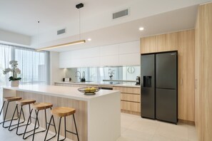 A modern kitchen with a central island, bar stools, a black refrigerator, and wooden cabinets.