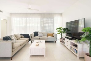 A modern living room with a sofa, coffee table, TV stand, and large windows.