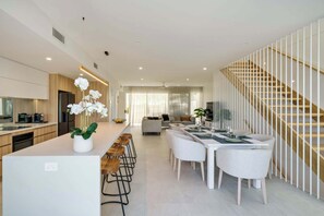 A modern kitchen with a central island, bar stools, and a dining area with a staircase.