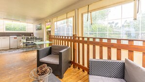 Ein überdachter Patio-Bereich mit Korbmöbeln, einer Holzterrasse und Blick ins Grüne.