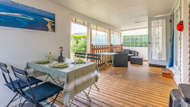 Eine überdachte Terrasse mit Esstisch, Stühlen und einer Couch.