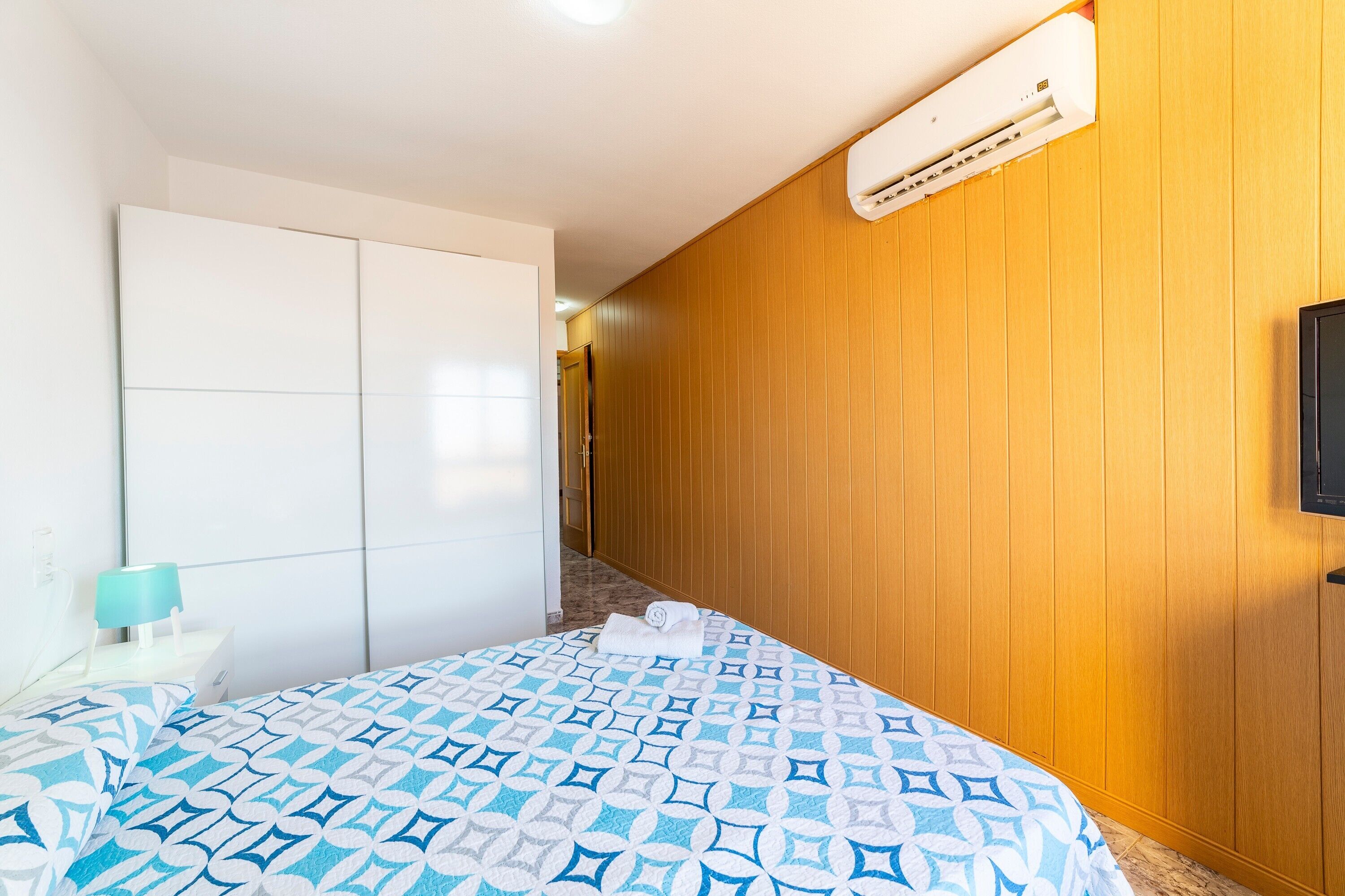 Una habitación de hotel con una cama, un televisor, un equipo de aire acondicionado y una pared de madera.