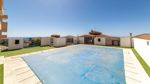 Una piscina en la azotea con cubierta azul, rodeada por un edificio blanco con tejado de baldosas, bajo un cielo despejado.