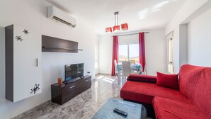 Una sala moderna con televisor de pantalla plana, un sofá rojo, una mesa de centro y un comedor al fondo.