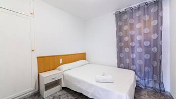 Una cama individual con cabecera de madera, una mesita de noche y una cortina gris con estampado de lunares.