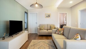 A living room with a flat-screen TV, a sofa, a patterned rug, and a pendant light. - Apartment 'Referta Apartamento T1' with Sea View, Private Terrace and Wi-Fi (Prazeres)