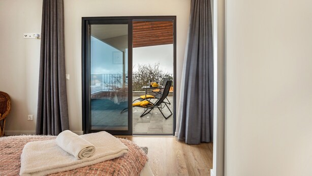 A bedroom with a bed, a window, a sliding glass door leading to an outdoor area with a chair and a table. - Apartment 'Referta Apartamento T1' with Sea View, Private Terrace and Wi-Fi (Prazeres)