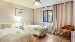 A hotel room with two beds, a wicker chair, a window with curtains, a picture on the wall, and a lamp. - Holiday Home 'Referta House' with Sea View, Private Garden and Wi-Fi (Prazeres)