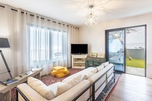 A modern living room with a sofa, TV, and a balcony with a view.