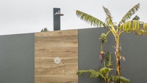 A modern building with a wooden panel wall, a grey wall, and a plant with hanging bananas. - Holiday Home 'Referta House' with Sea View, Private Garden and Wi-Fi (Prazeres)
