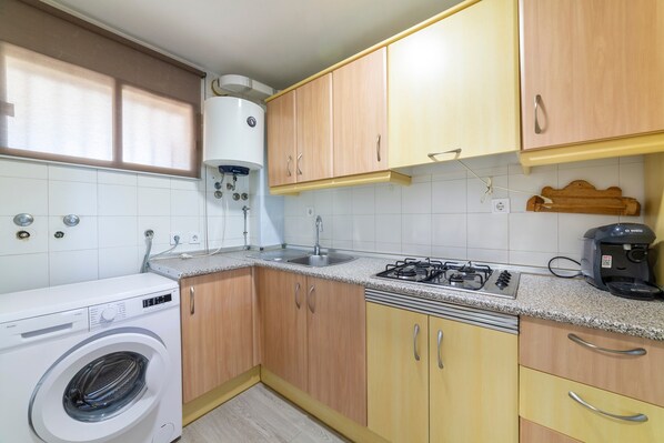 Une cuisine compacte équipée d’un lave-linge, d’une cuisinière à gaz et de meubles de rangement en bois.
