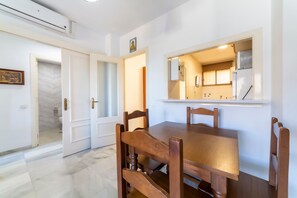 Un coin repas avec une table et des chaises en bois, une cuisine équipée d’un réfrigérateur et d’une cuisinière, et une salle de bain avec des toilettes et une douche.