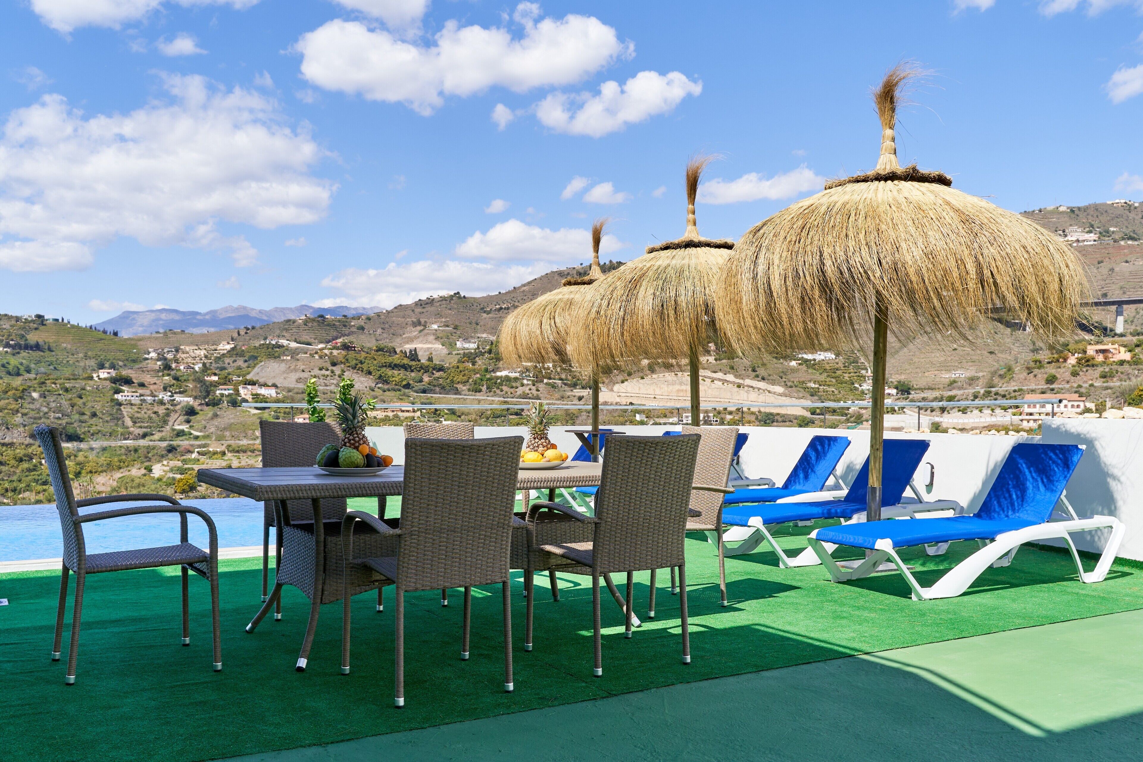 A terrace with a table, chairs, and umbrellas overlooking a scenic landscape.