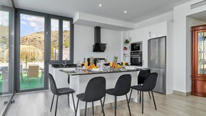 Een moderne keuken met een centraal kookeiland, roestvrijstalen apparatuur en uitzicht op een heuvel.