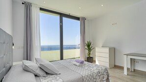 Een slaapkamer met een bed, een bureau, een potplant en uitzicht op zee.