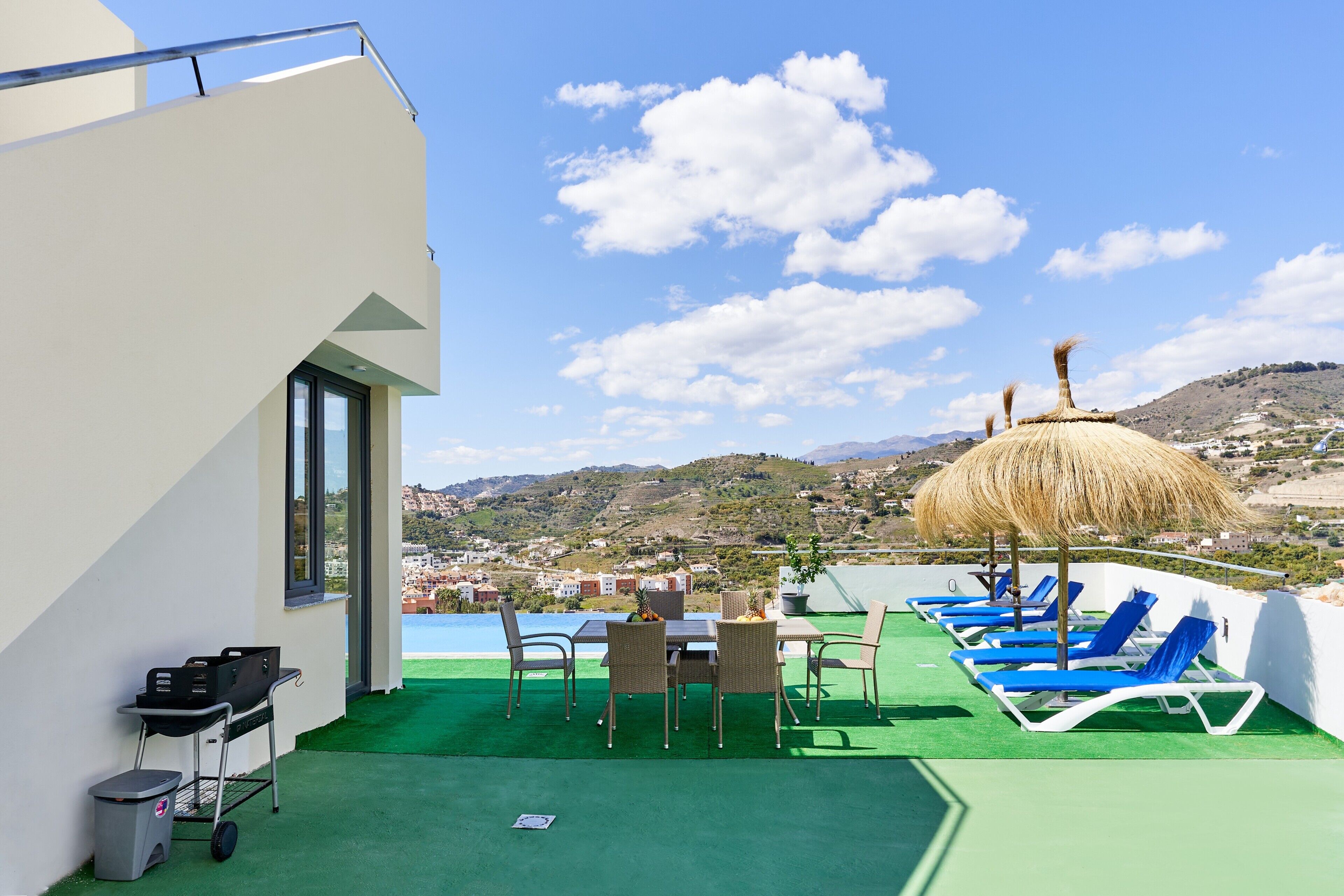 A rooftop terrace with a pool, lounge chairs, a table, and a thatched umbrella.