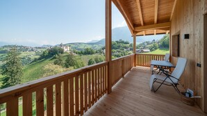 A wooden balcony with a table and chairs, overlooking a scenic landscape with a castle and rolling hills. - Apartment "Schlosshof Himml" with Mountain View, Private Terrace & Wi-Fi (Fiè allo Sciliar)