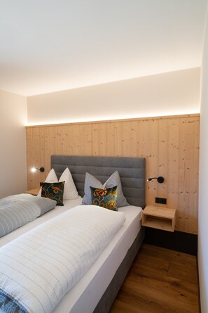 Une chambre moderne avec une tête de lit en bois, un lit agrémenté de plusieurs oreillers, une table de chevet et une lampe fixée au mur.