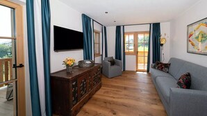 A living room with a grey sofa, wooden cabinet, flat-screen TV, and a painting on the wall. - Apartment "Schlosshof Himml" with Mountain View, Private Terrace & Wi-Fi (Fiè allo Sciliar)