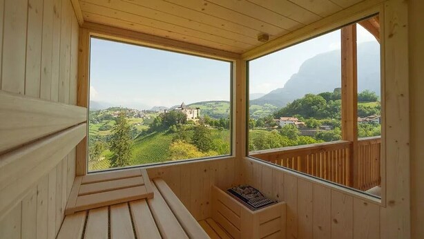A wooden room with a large window offering a view of a castle and surrounding greenery. - Apartment "Schlosshof Himml" with Mountain View, Private Terrace & Wi-Fi (Fiè allo Sciliar)