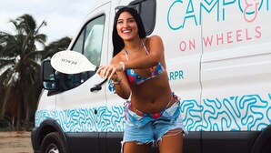 Een persoon staat voor een wit voertuig met blauwe en roze patronen en de tekst 'CAMPO ON WHEELS'.