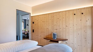 Una habitación de hotel moderna con un panel de pared de madera, una cama con edredón blanco y gris, una pequeña mesa de madera y una silla.