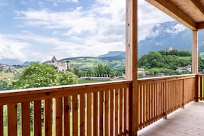 Ein Holzbalkon mit Blick auf ein Schloss, grüne Hügel und einen Berg im Hintergrund.