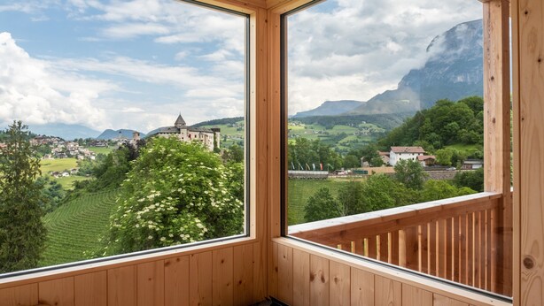 Una habitación con paredes de madera y ventanas amplias que dan a una vista de un pueblo, montañas y una iglesia.