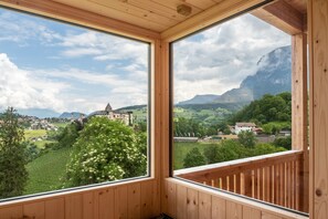 A room with wooden walls and large windows offering a view of a village, mountains, and a church. - Apartment "Schlosshof Hoamat" with Mountain View, Terraces & Wi-Fi (Fiè allo Sciliar)