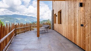 Una terraza de madera con sillones de descanso, un muro de piedra y vistas a las montañas.