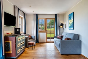 Ein Wohnzimmer mit einer Couch, einem Fernseher, einem Holzschrank und Blick ins Freie.