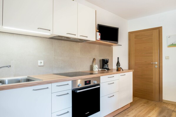 A modern kitchen with white cabinets, a stainless steel sink, a Bosch oven, and a flat-screen TV mounted above the stove.